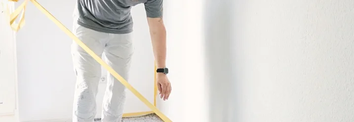 Person klebt Malerband an eine Wand